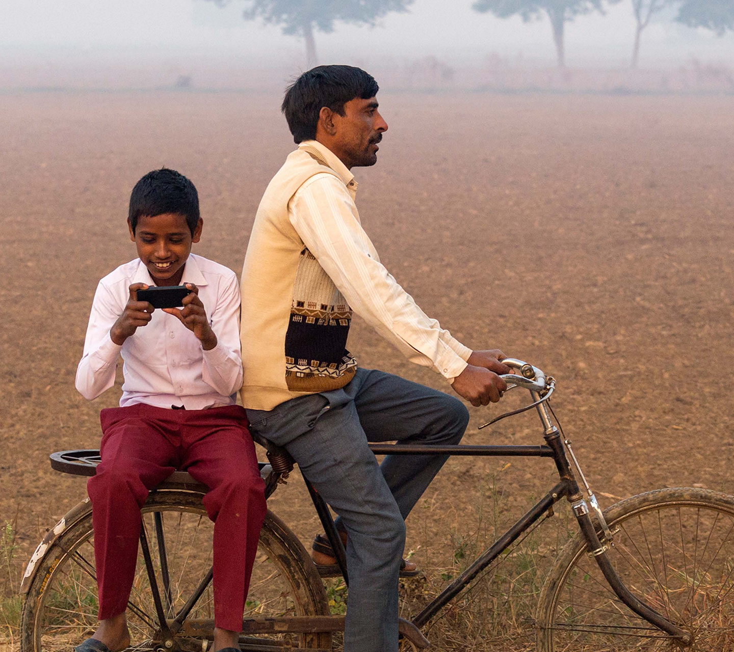 South Asian father and son cycling past a field